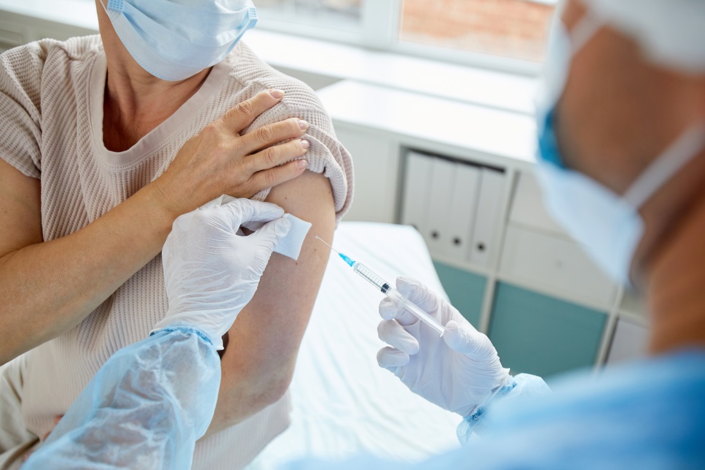 Modern medical worker giving injection with vaccine to unrecognizable female patient into shoulder, high angle view shot